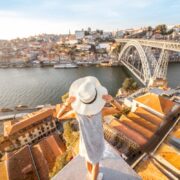 Young woman tourist enjoying beautiful landscape view on the old town with river and famous iron bridge during the sunset in Porto city, Portugal